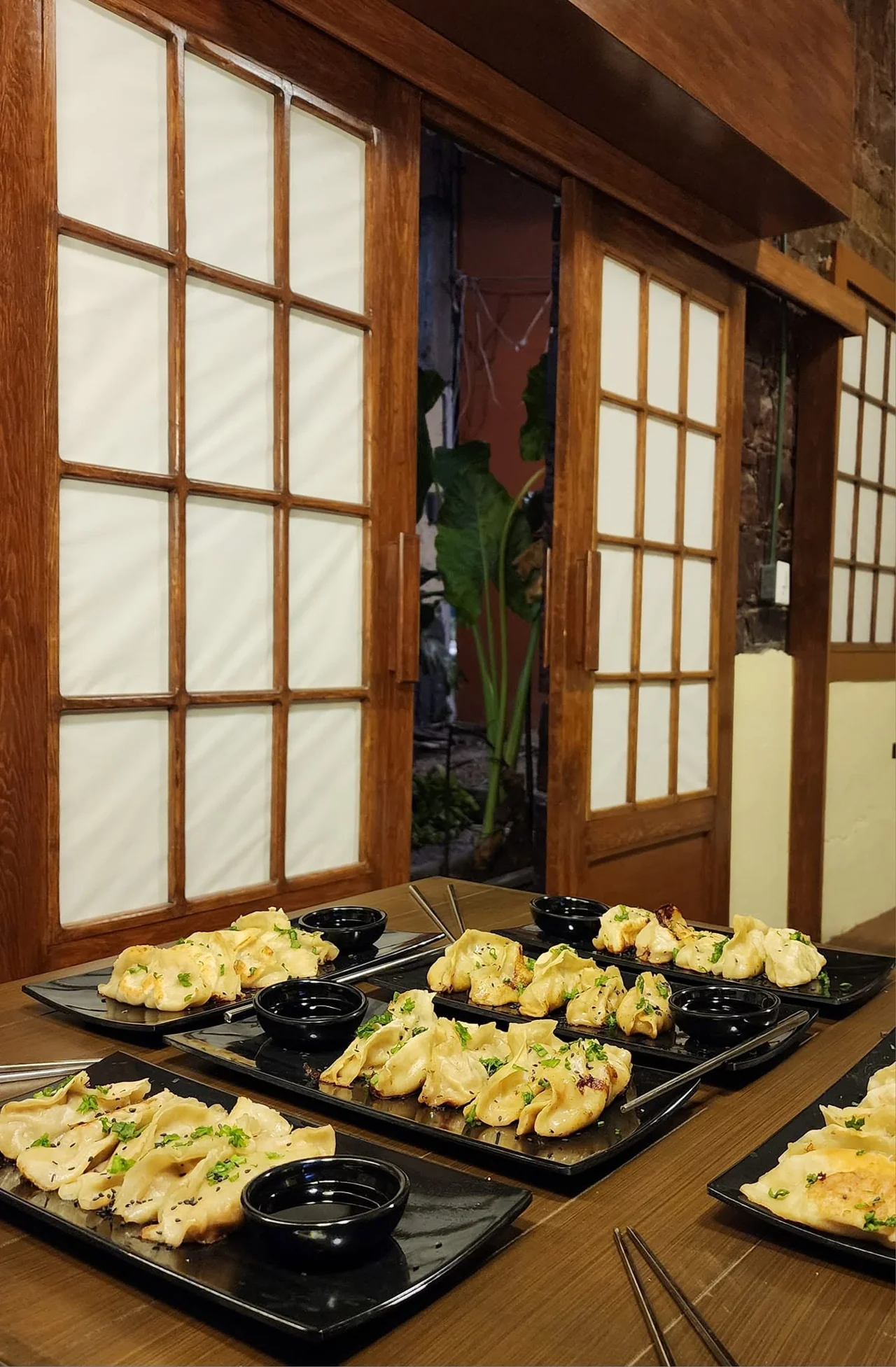 Platillos orientales en vajilla negra sobre una mesa de madera, junto a los paneles del restaurante
